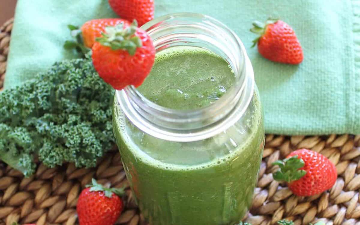 Strawberry orange kale smoothie with strawberry garnish in a mason jar.