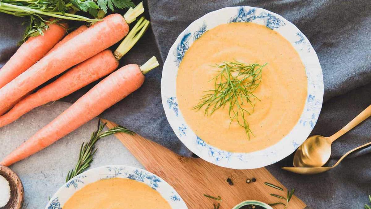 Creamy carrot soup with fennel and white beans in a blue and white bowl.