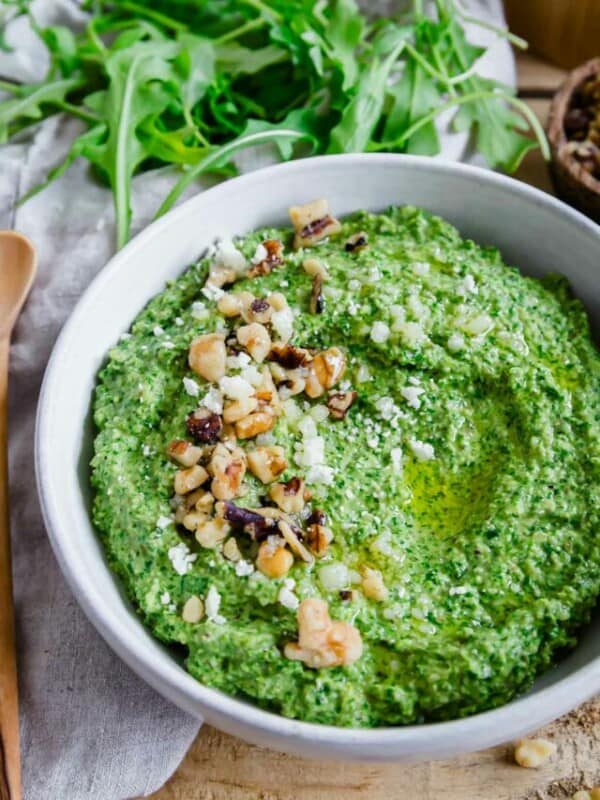 A bowl of pesto hummus with walnuts and pine nuts.