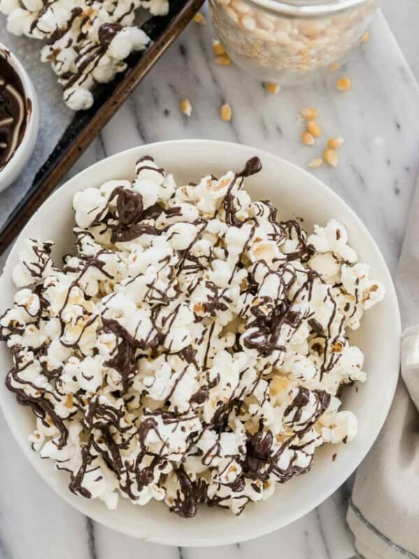 A bowl of popcorn with chocolate drizzle and peanuts.
