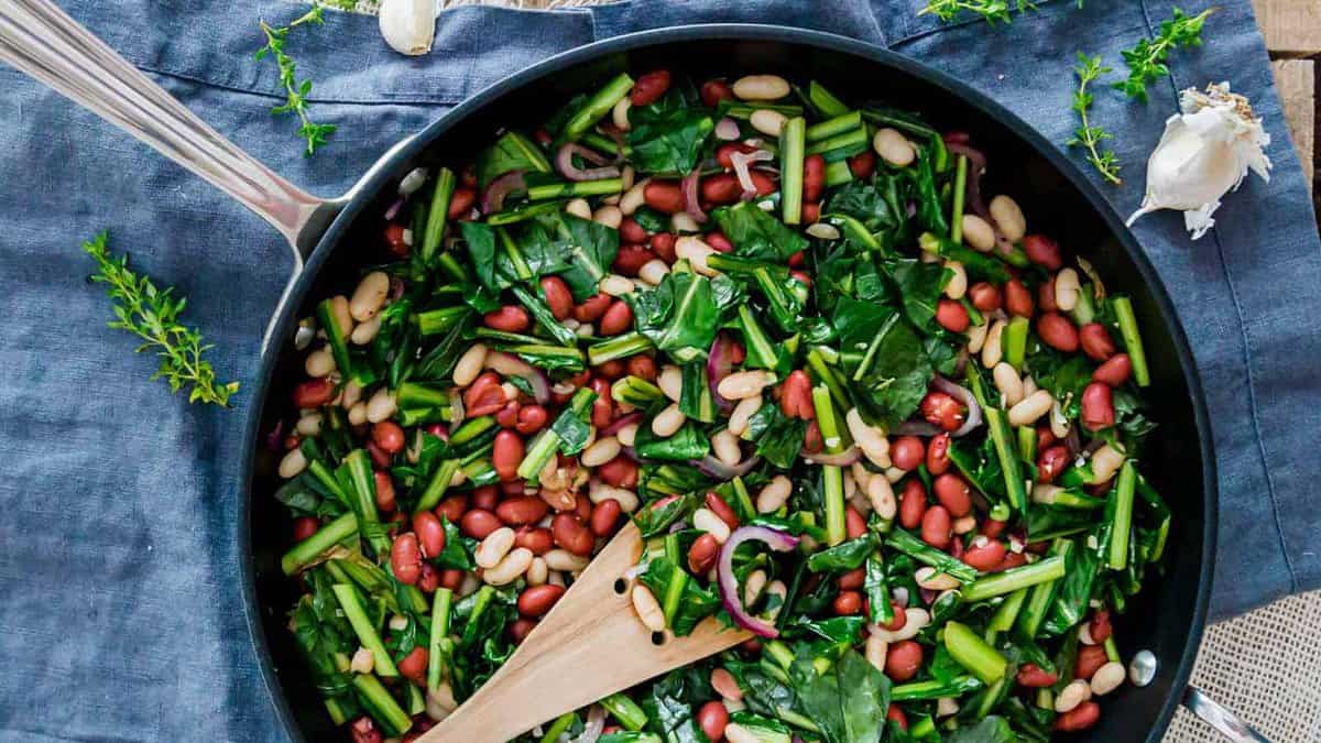 Beans and greens in a skillet with a wooden spoon.