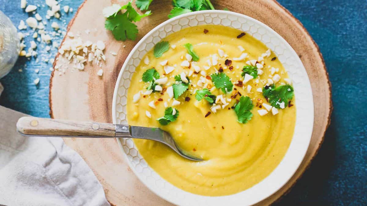 A bowl of delicata squash soup with a spoon on a wooden table.