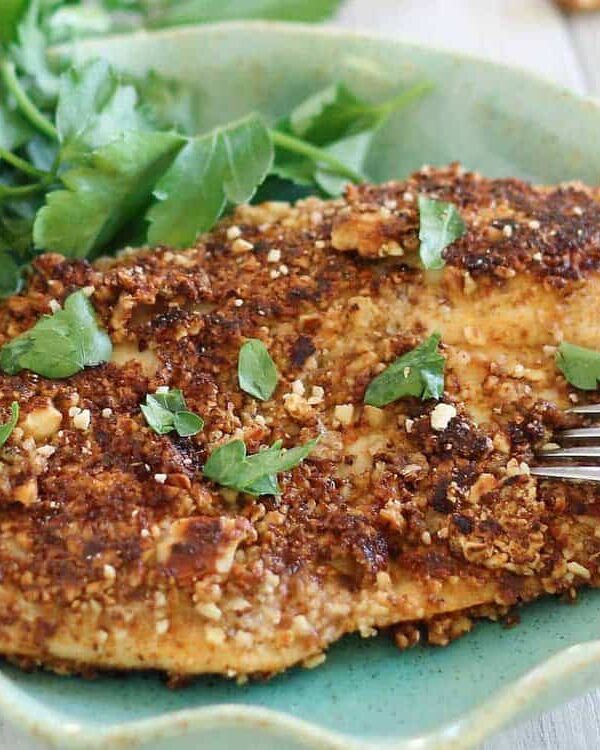 Almond crusted tilapia on a green plate with parsley.