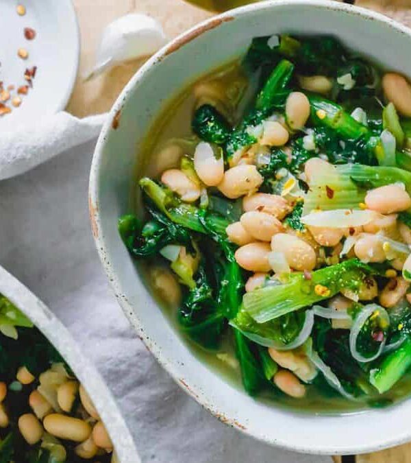 Two bowls of white beans and green beans on a wooden table.