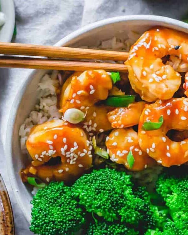 A bowl of shrimp and broccoli with chopsticks.