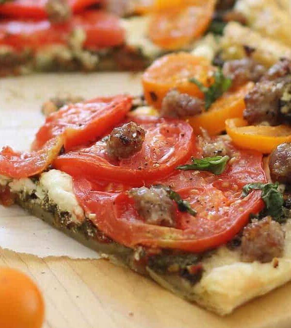 A slice of tomato and sausage tart on a cutting board.
