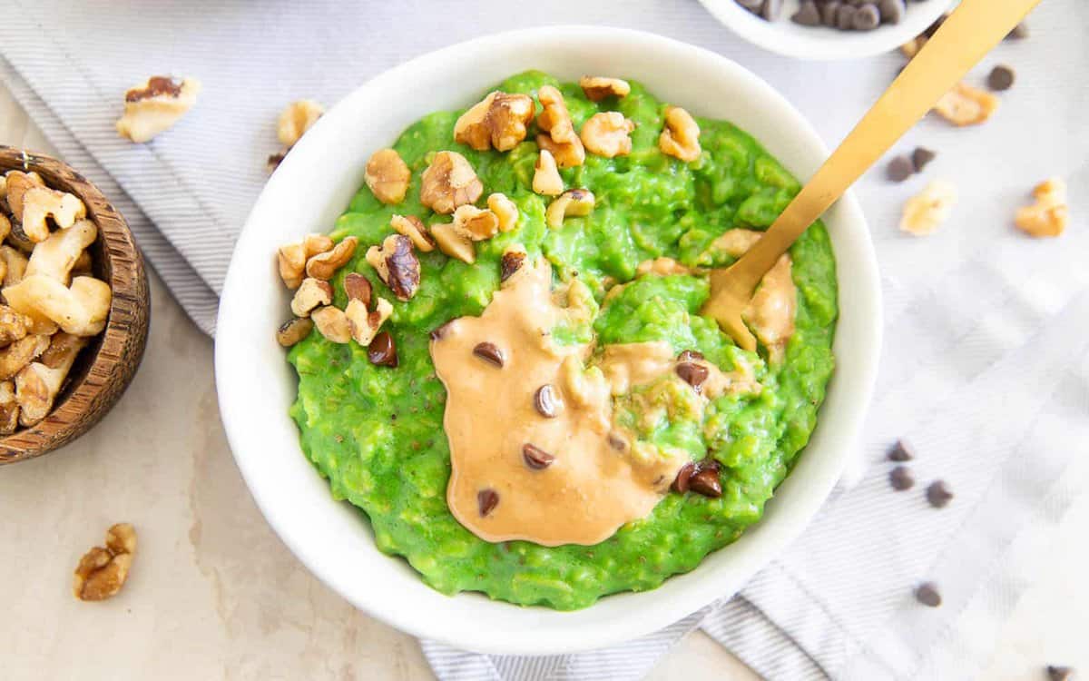Green oatmeal in a bow with nut butter and chopped nuts.