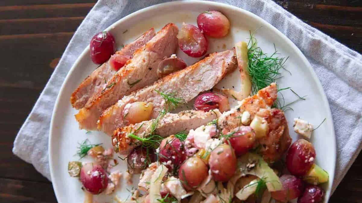 Grilled pork chops sliced on a plate with grapes and fennel.