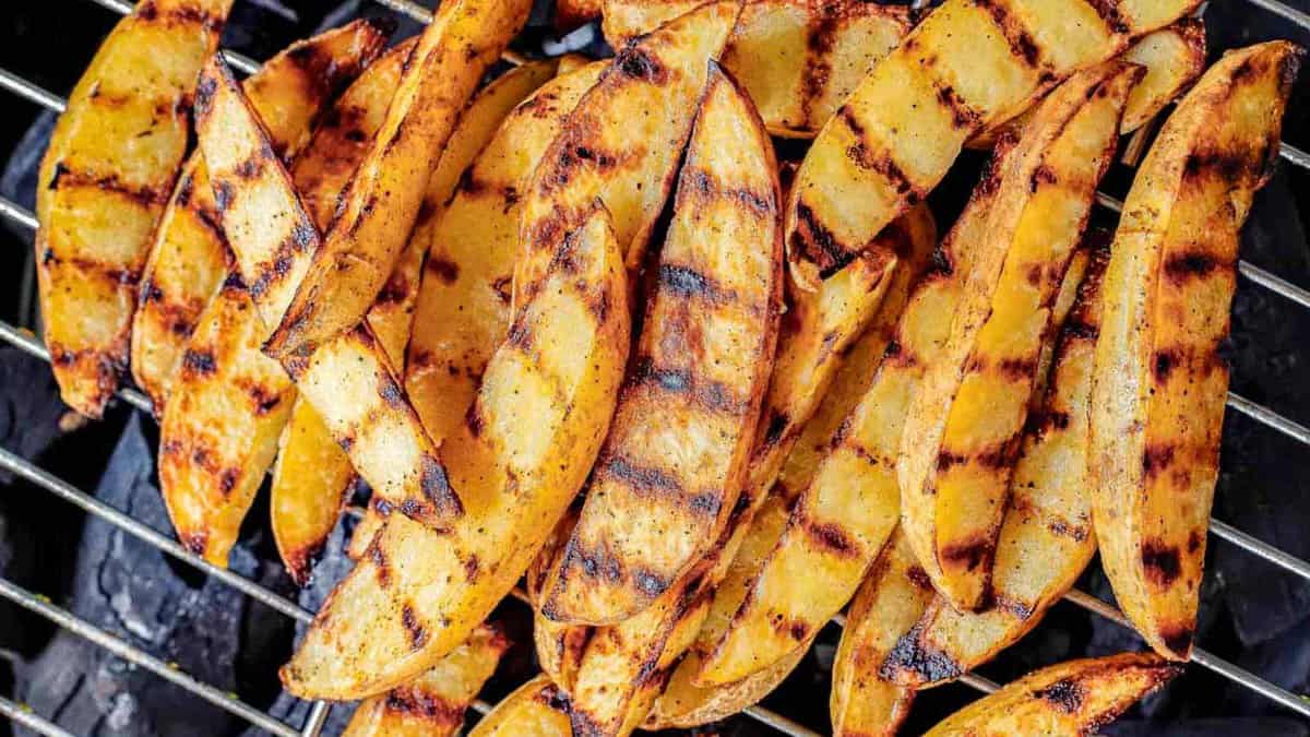 Grilled potato wedges on grates of charcoal grill.