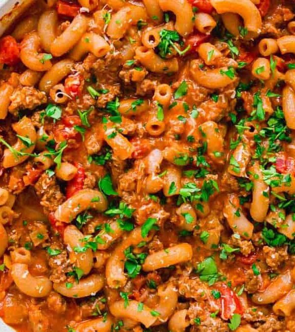 Pasta with meat and tomatoes in a white dish with a wooden spoon.