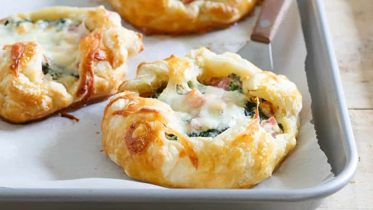 Mini ham and cheese spinach breakfast pies on a baking sheet.