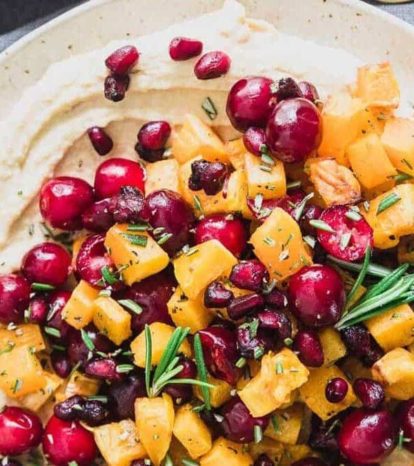 A plate of hummus with cranberries and sprigs of rosemary.