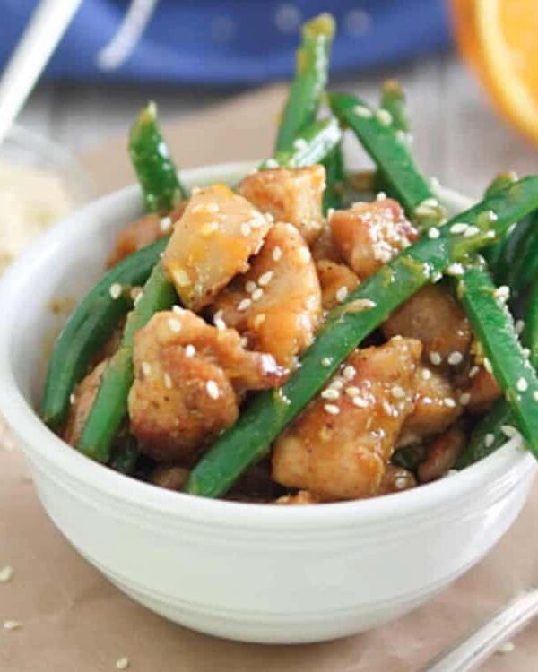 Chicken and green beans in a white bowl with orange slices.