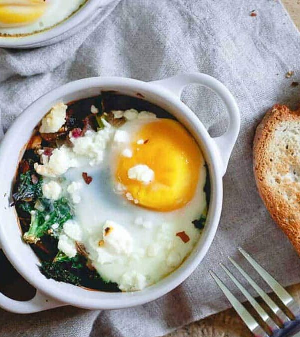 Two bowls of eggs with spinach and bread on a table.