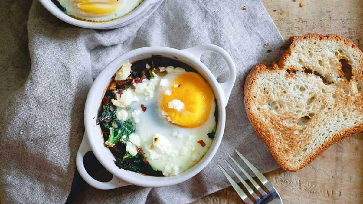 Kale and feta egg bake in a white ramekin with a piece of toasted bread to the side.