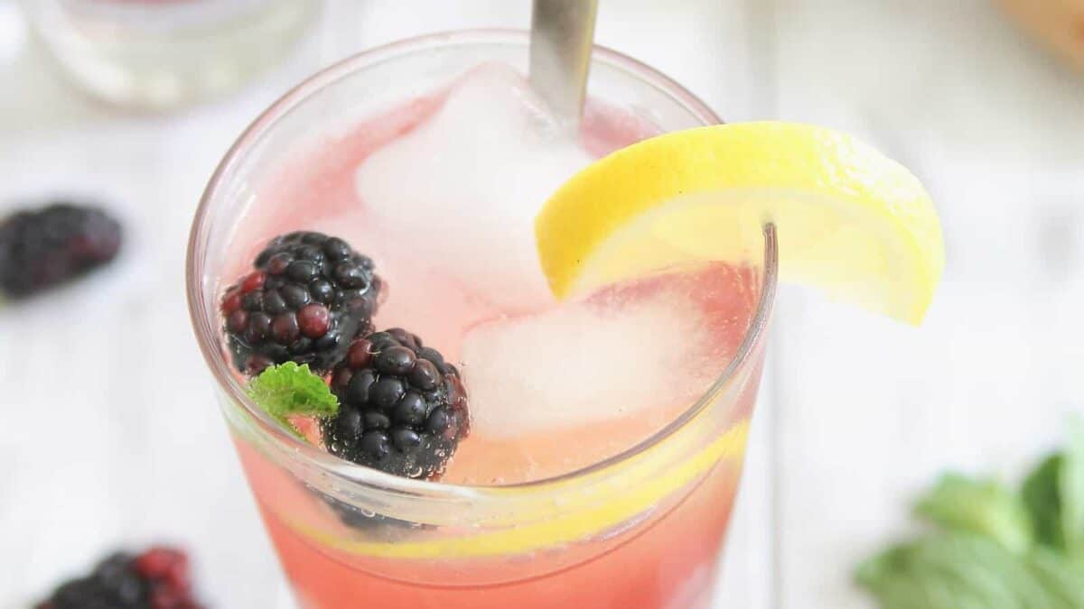 A glass of blackberry lemonade with ice and mint.