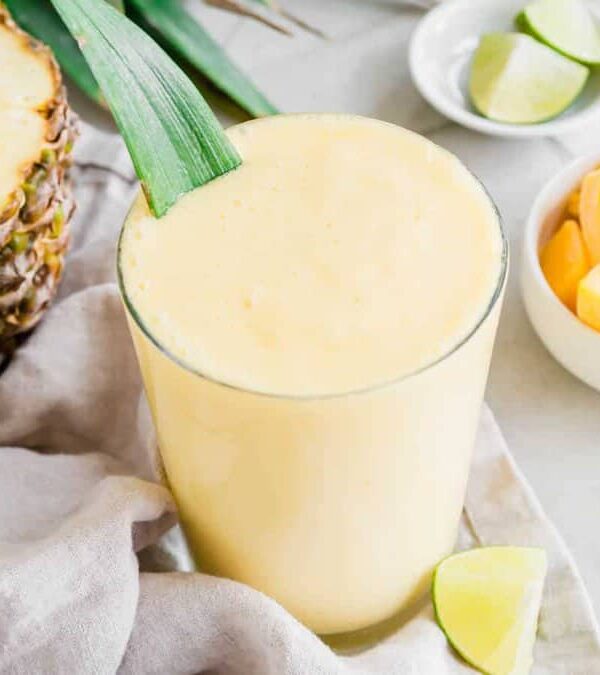A pineapple mango smoothie with a slice of lime and a slice of pineapple.