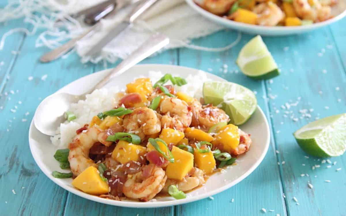 Mango shrimp served with white rice on a white plate with spoon.