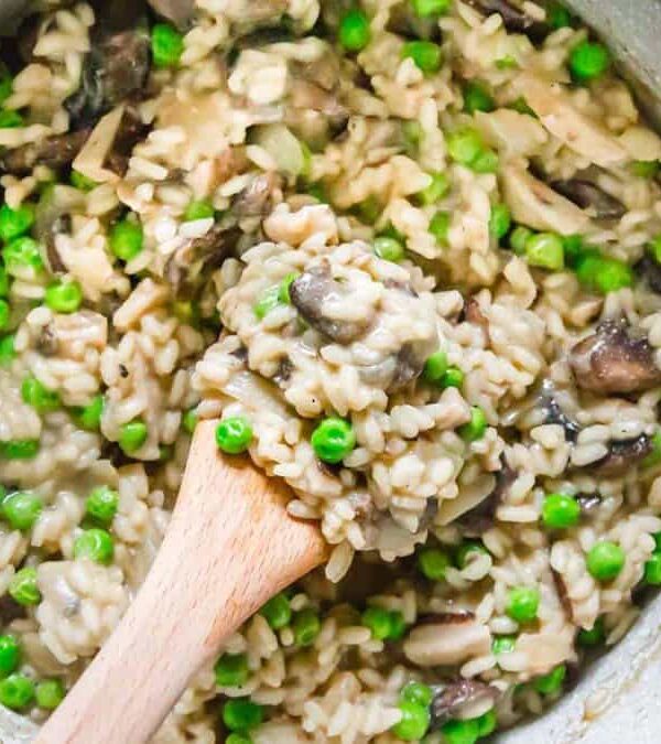 Mushroom and pea risotto in a pan with a wooden spoon.