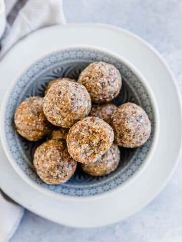 Oat almond date energy balls in a bowl with a bite taken out of one on top.