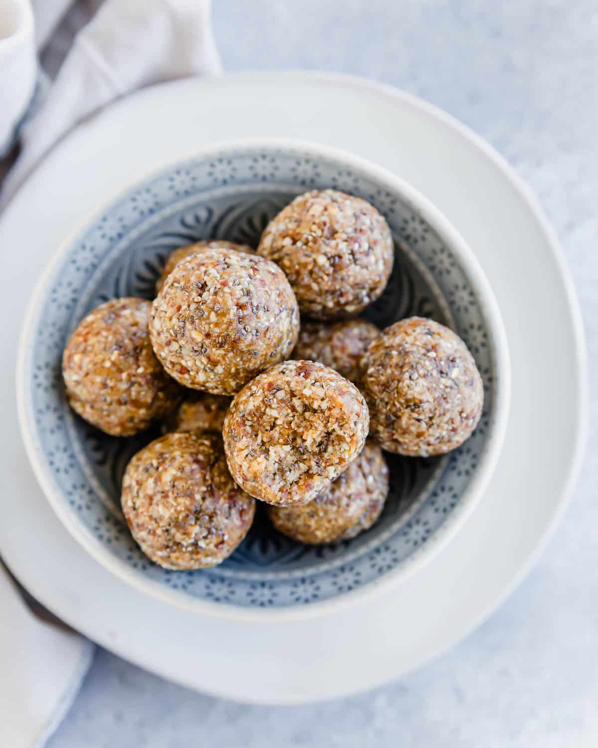 Oat almond date energy balls in a bowl with a bite taken out of one on top.