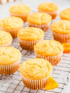 Orange muffins in parchment paper wrappers on a cooling rack.