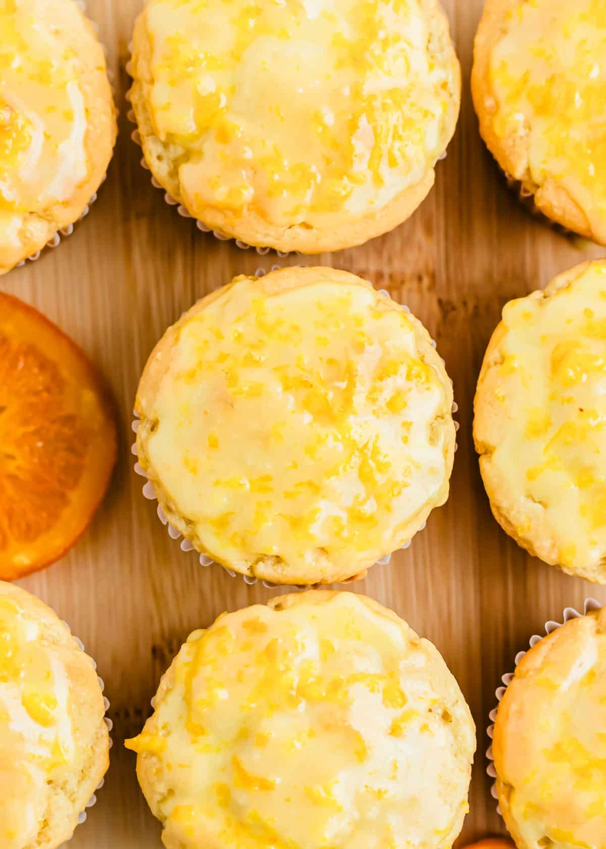 A wooden cutting board with orange glazed muffins on it.