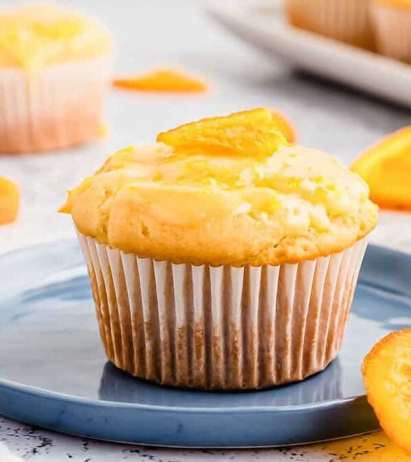 A baked orange glazed muffin topped with candied orange on a blue plate.