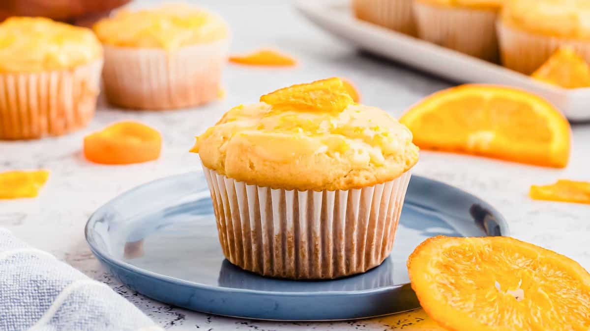A baked orange glazed muffin topped with candied orange on a blue plate.