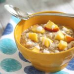 Peach oatmeal in a yellow bowl with a spoon.