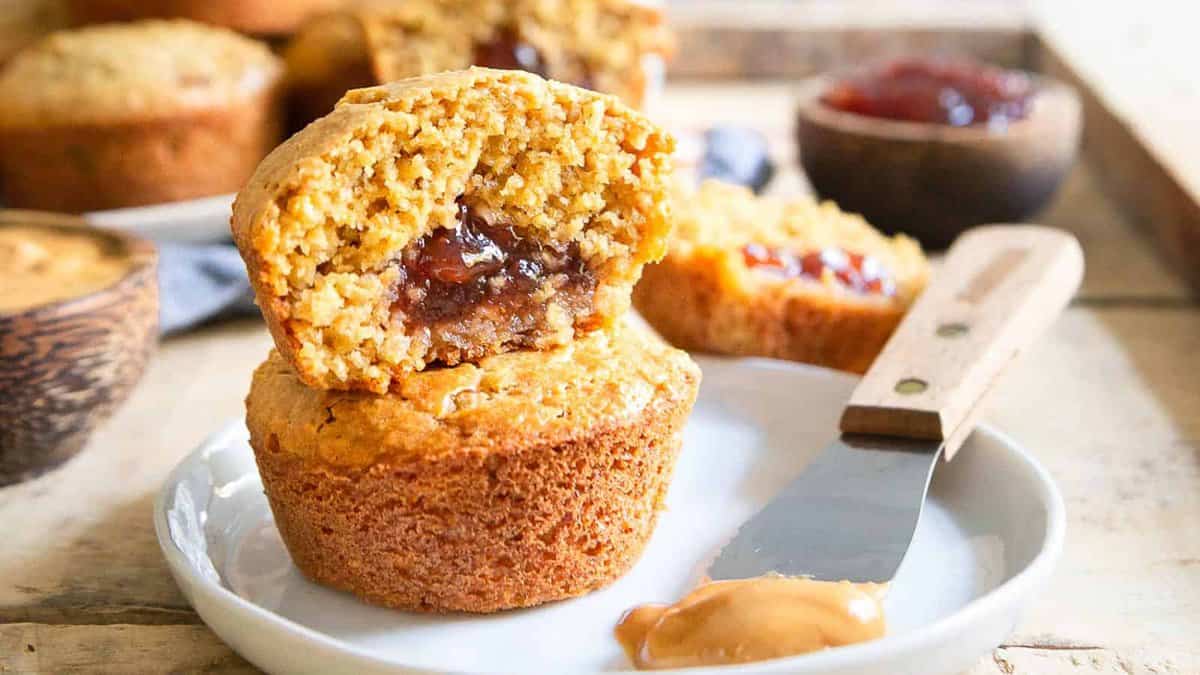 Peanut butter and jelly muffins on a plate with a spatula with peanut butter.