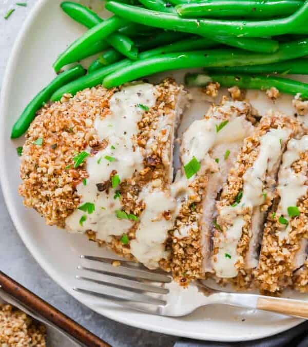 A plate with pecan crusted chicken breasts and green beans on it.