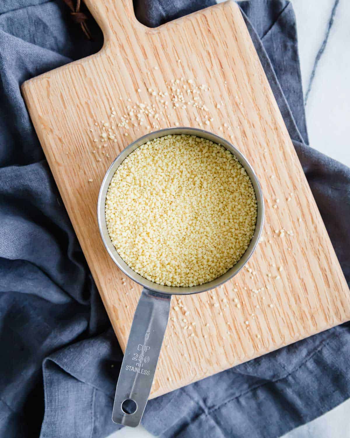 Couscous in a measuring cup on a wooden cutting board.