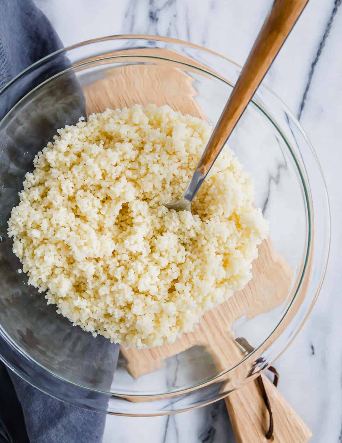 Couscous in a glass bowl with a wooden fork.