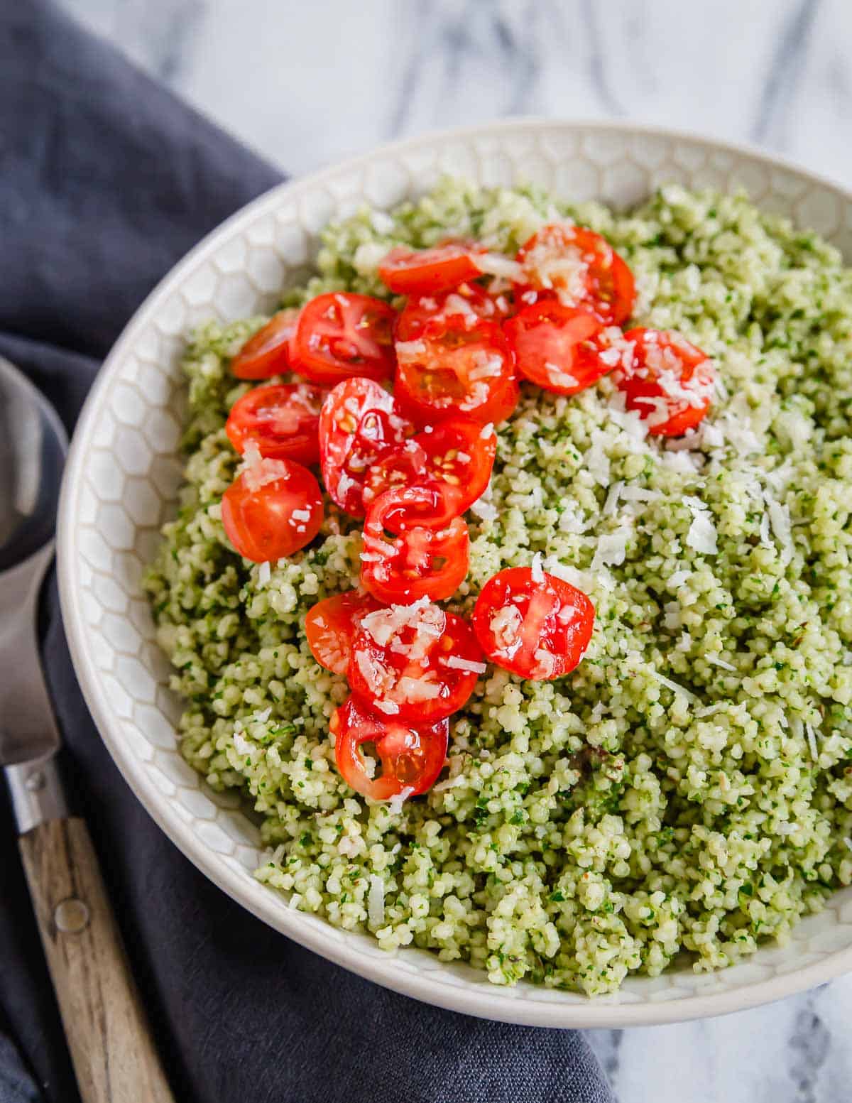A bowl of green pesto couscous with tomatoes and parmesan cheese.