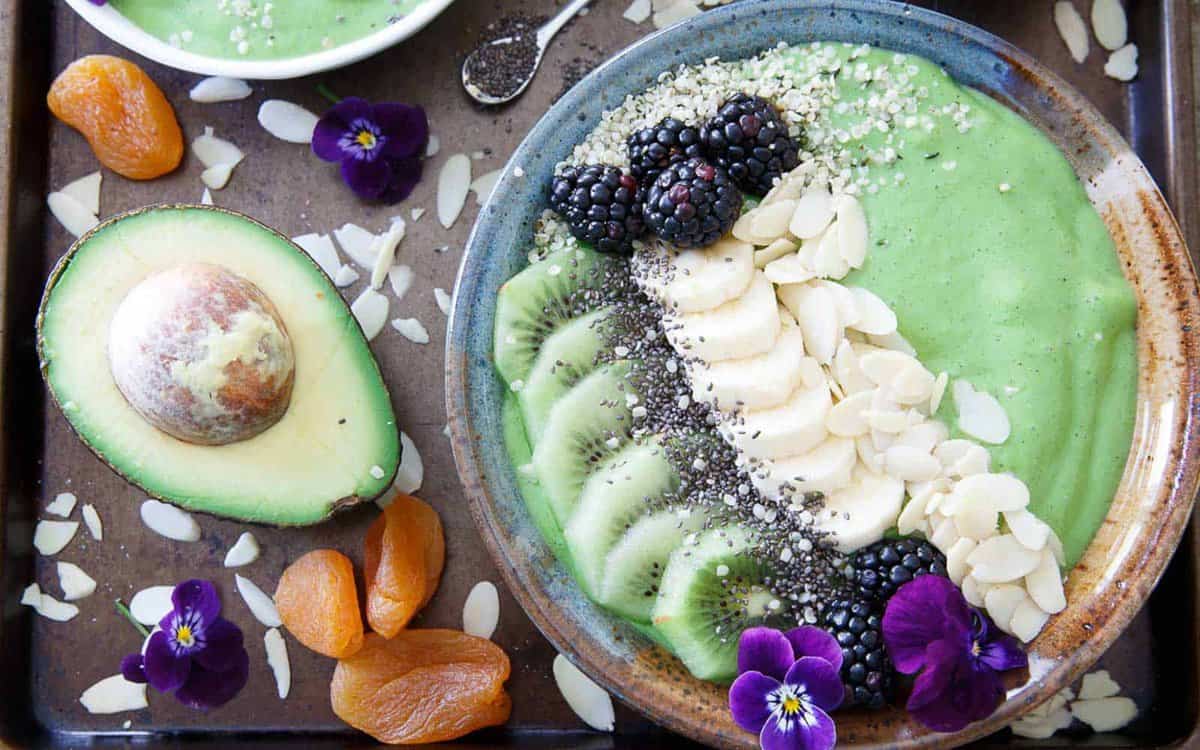 Avocado pineapple smoothie bowl with kiwi, banana and edible flower garnish.