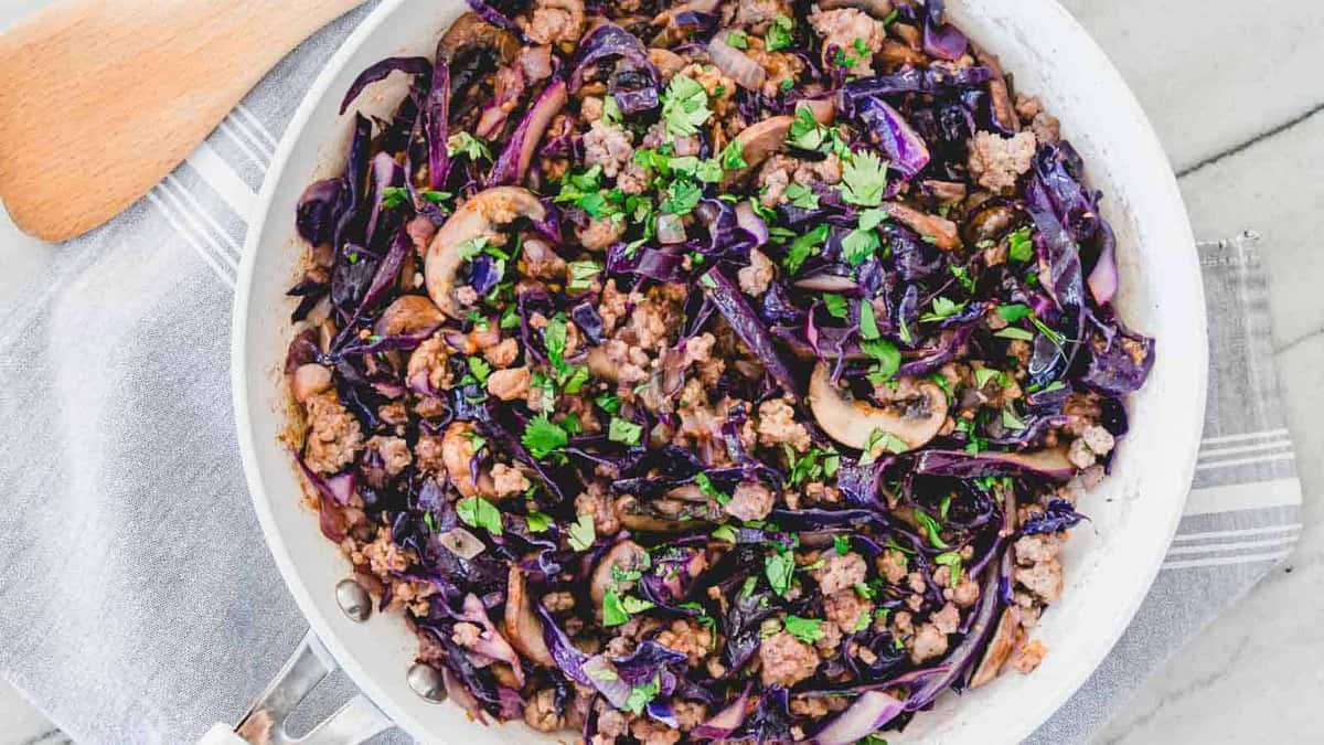 Ground pork and purple cabbage stir fry in a white pan.