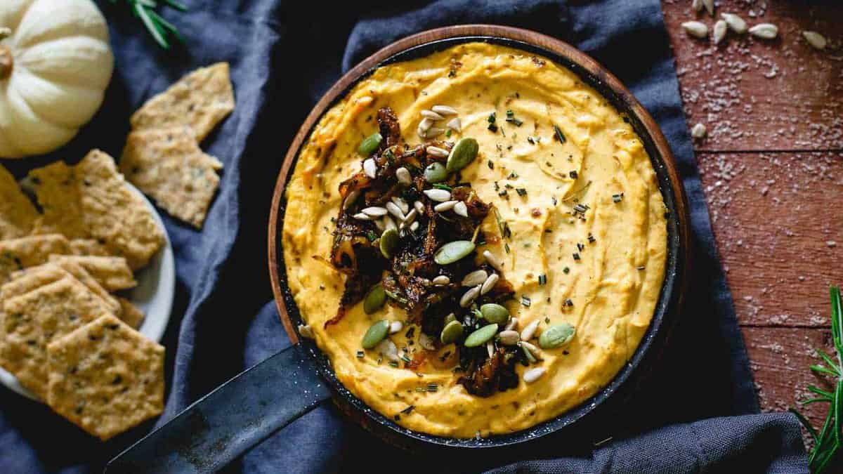 Pumpkin goat cheese dip topped with caramelized onions, sunflower seeds and pepitas in a small skillet.