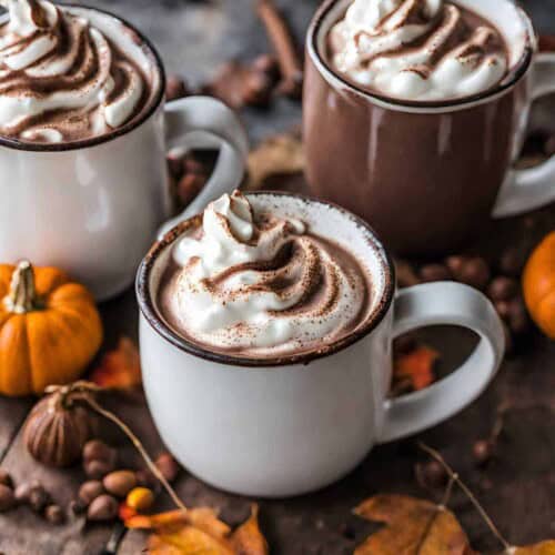 Three mugs of hot chocolate with whipped cream and pumpkins.