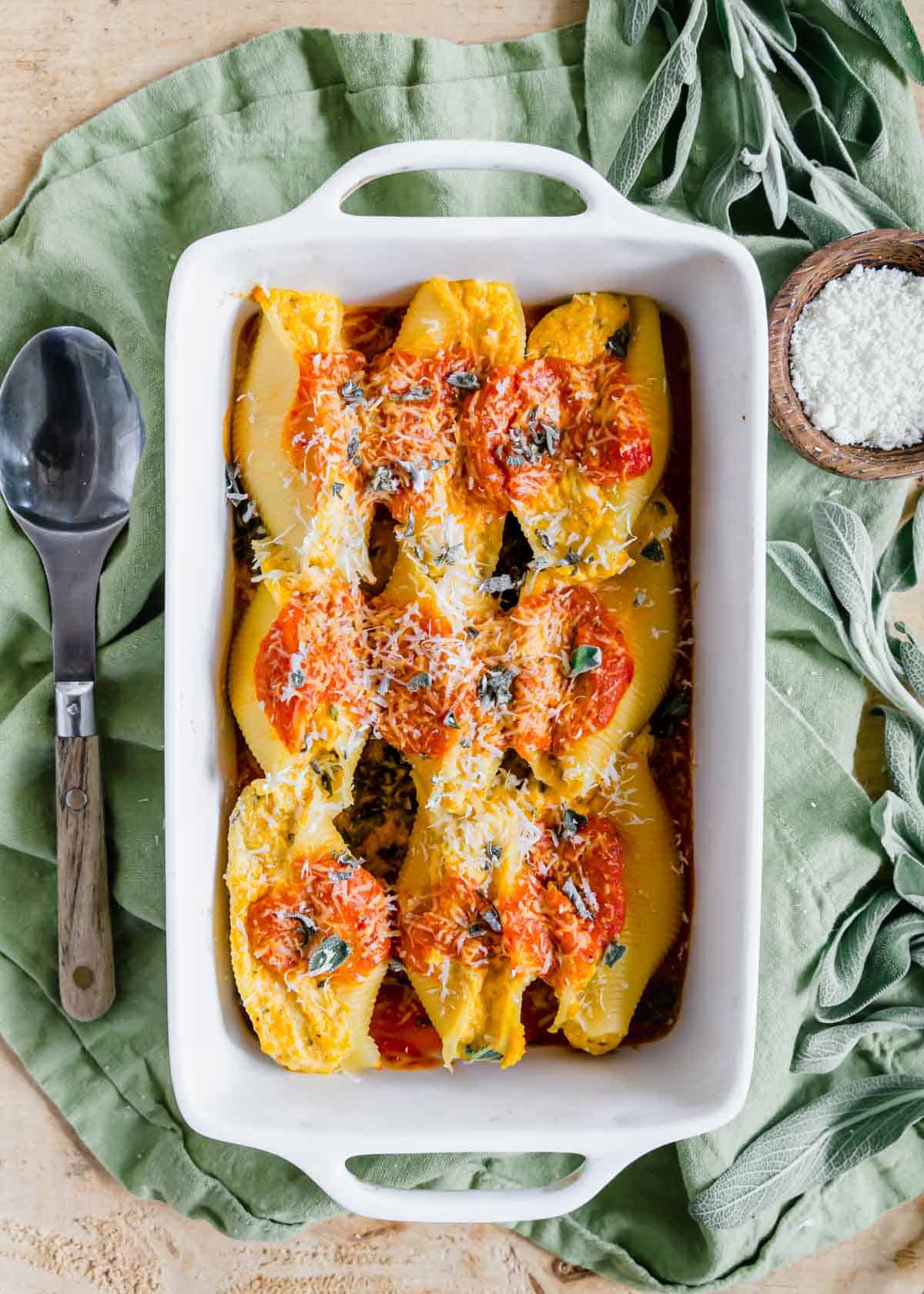 Pumpkin stuffed shells in a white baking dish with a serving spoon on the side.
