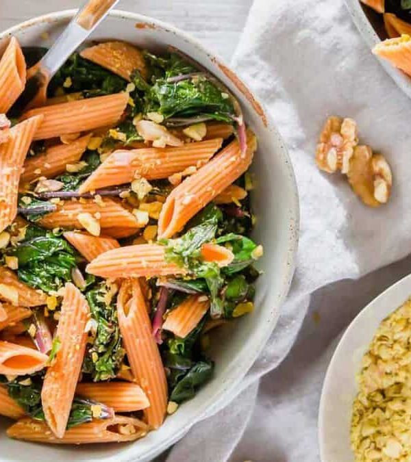 A bowl of pasta with greens and walnuts.