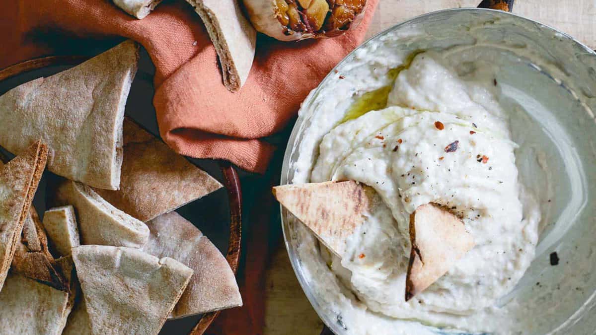 Roasted garlic white bean dip in a metal dish with pita chips.