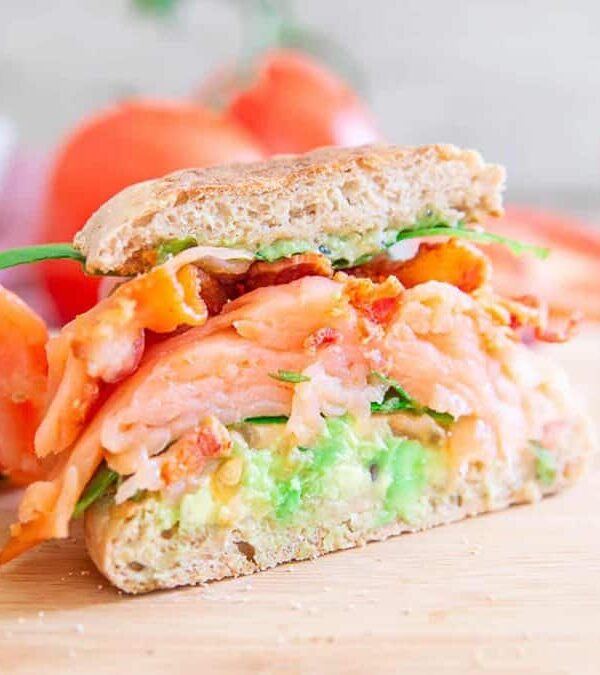 A salmon and avocado sandwich on a cutting board.