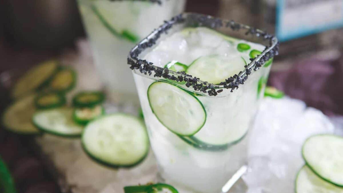 A cucumber margarita with ice cubes and cucumber slices.