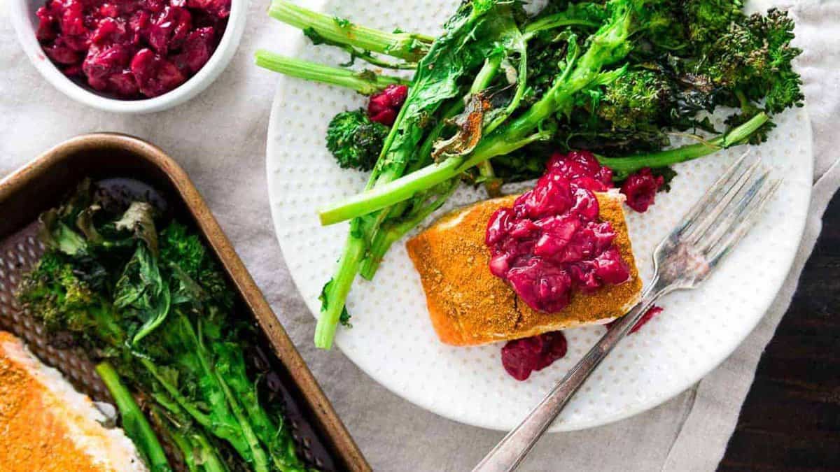 Turmeric salmon with cherry sauce and roasted broccoli rabe on a plate.