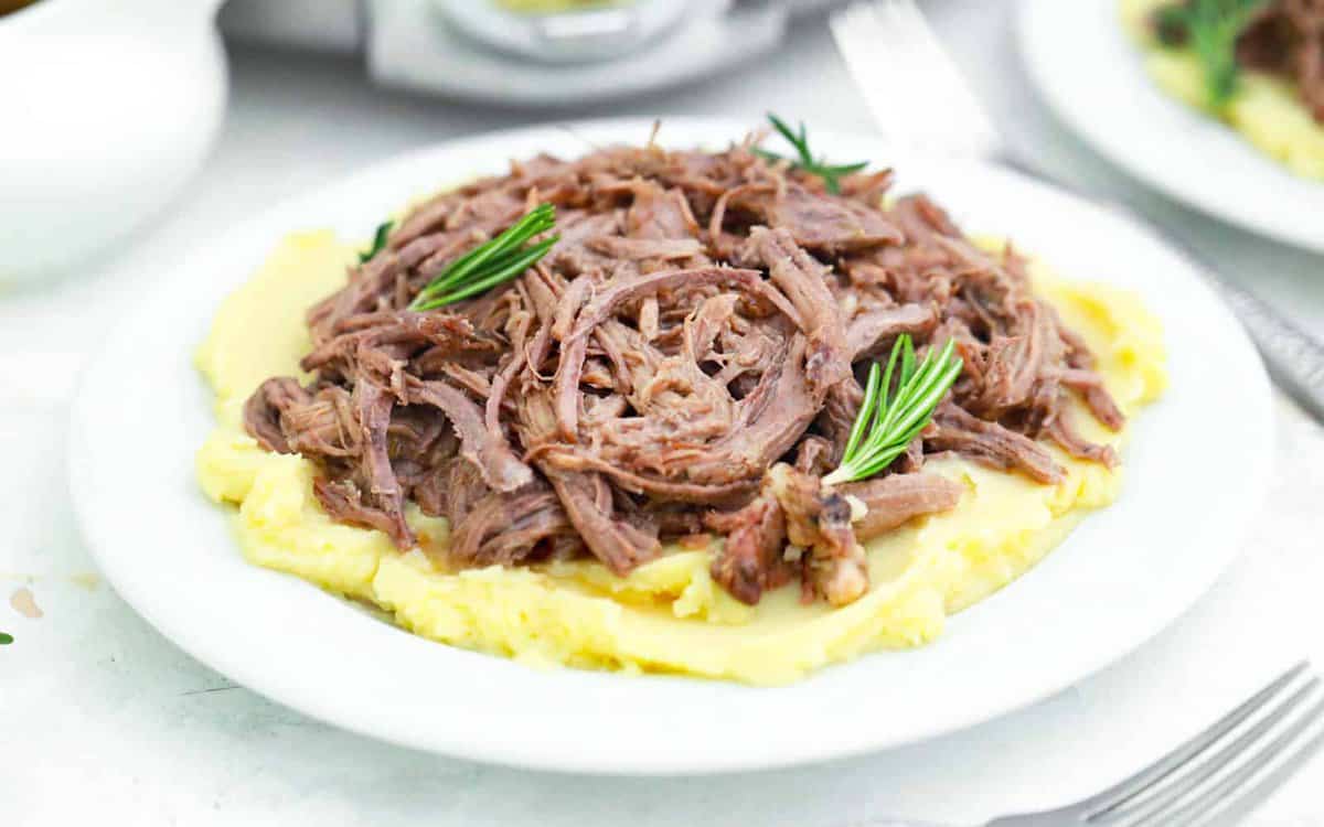 Slow cooker shredded tri tip in a white bowl over mashed potatoes.