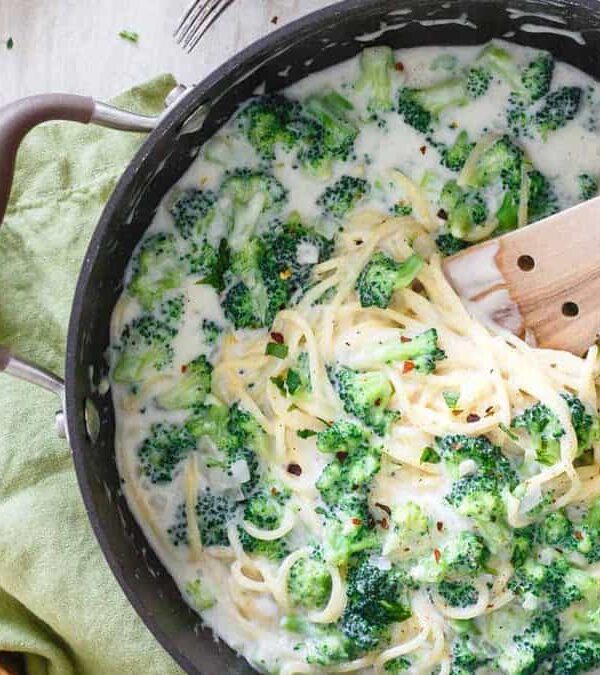 A pan full of pasta and broccoli with a wooden spoon.