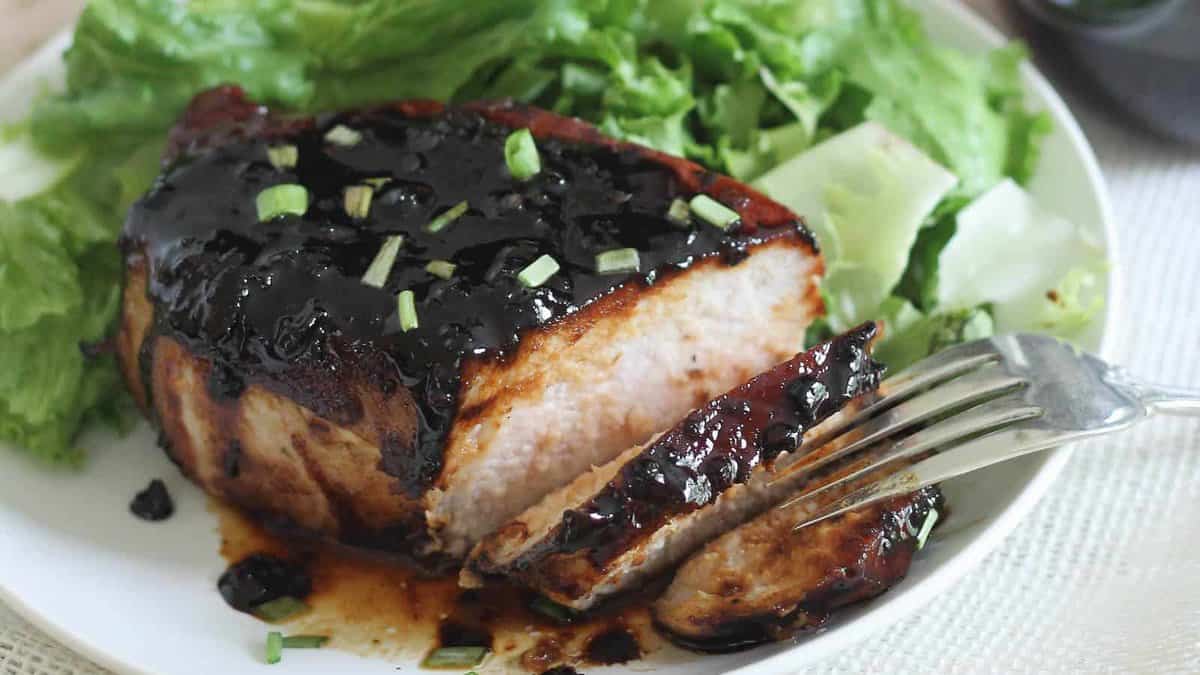 Pork chop glazed with sticky honey soy sauce and sliced on a plate with salad.