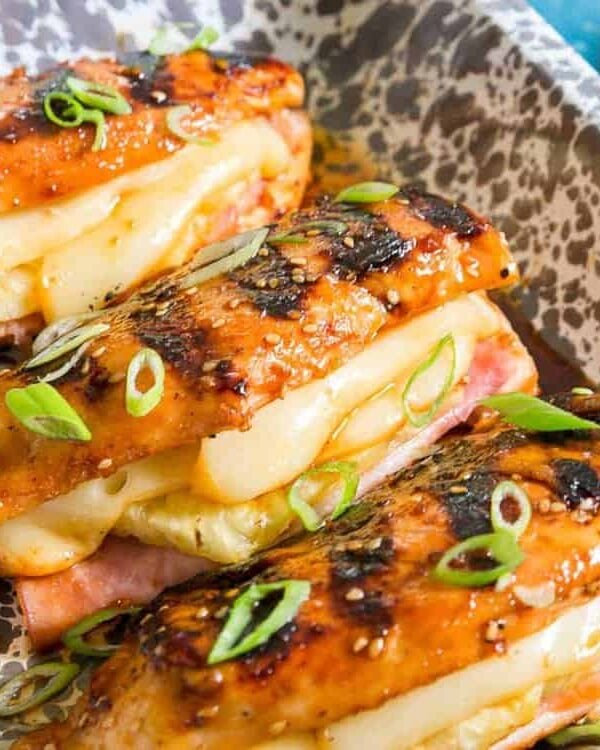 Three grilled chicken breasts on a plate stuffed with cheese, ham and pineapple.