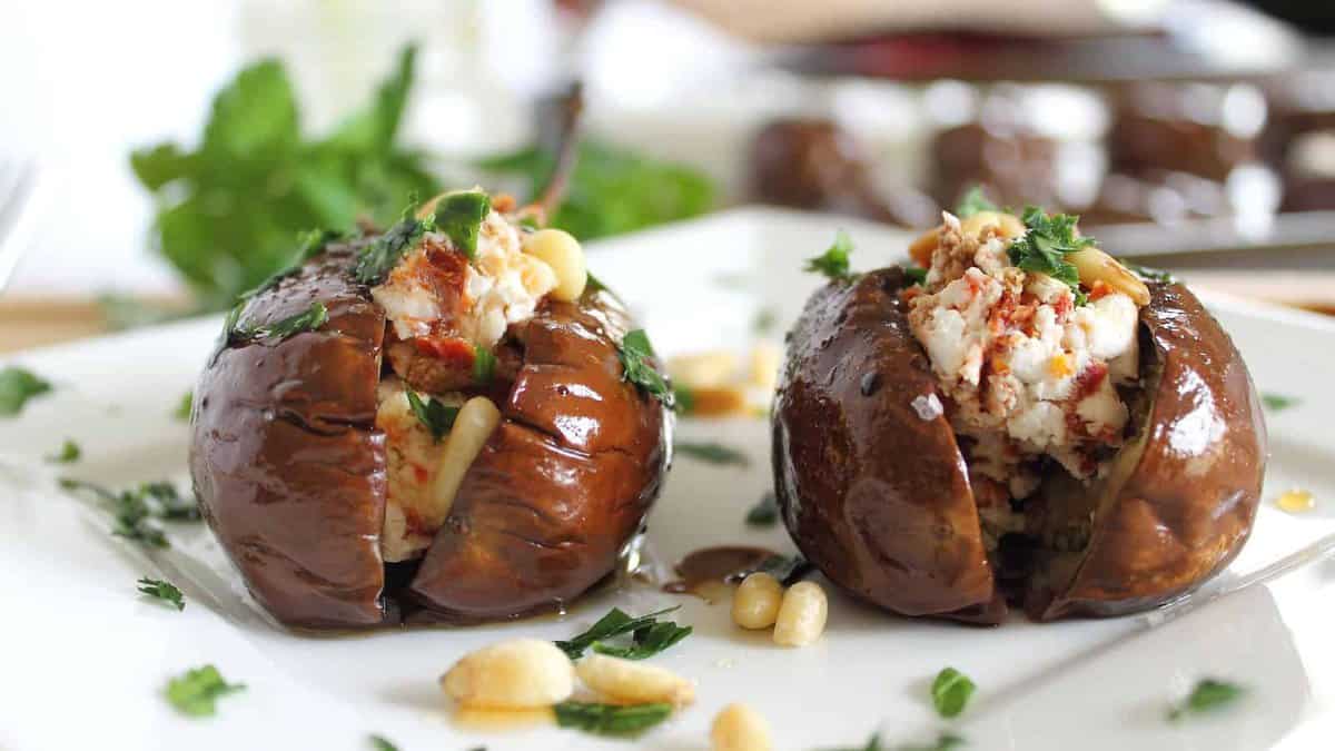Goat cheese stuffed baby eggplants on a white plate with parsley and pine nuts.